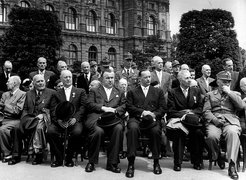 In Anzug und Uniform gewandete Männer sitzend bei einem Festakt, Schwarz-Weiß-Fotografie