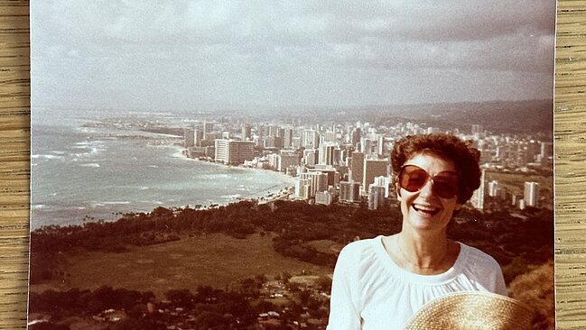 Retro Foto von lachender Person mit Sonnenbrille, im Hintergrund eine Stadt am Strand.