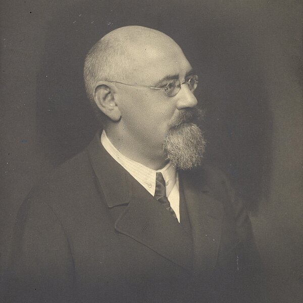 Seitliches Portrait eines Mannes mit Vollbart, Brille und Halbglatze, schwarz-weiß