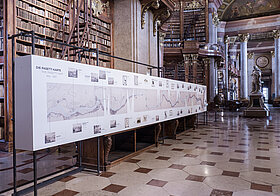 Stellage mit aufgedruckter Fluss-Karte in Marmorsaal vor Bücherregalen.