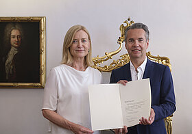 Zwei Menschen posieren mit einer Urkunde für ein Foto. 