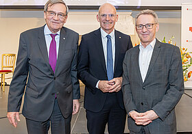 Drei Männer stehen lächelnd nebeneinander
