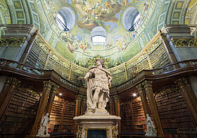 Große antike Statue in mitten einer barocken Bibliothek. 