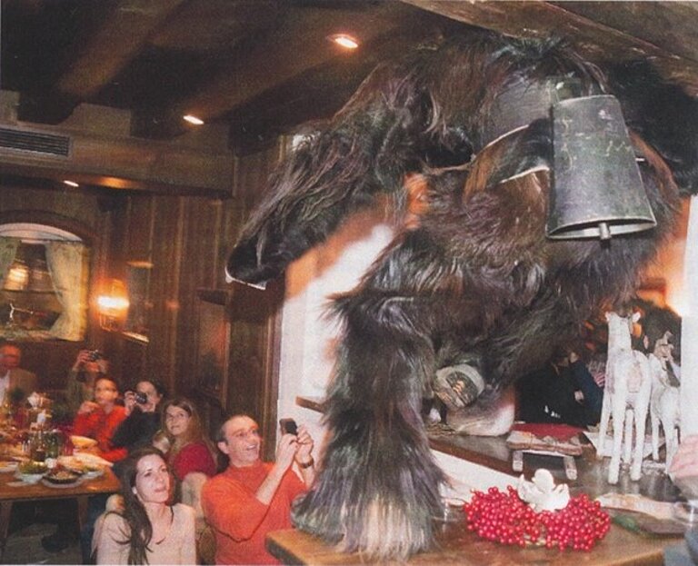 Person in Kostüm mit Pelz, die auf einem Tisch in einem Lokal steht, die Gäst*innen fotografieren sie.