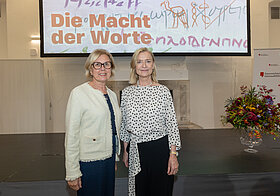 Zwei Personen stehen vor Bühne und Leinwand.