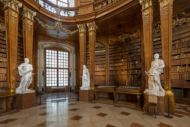 Foto von Marmorsaal mit zwei Statuen und prächtigen Bücherregalen.