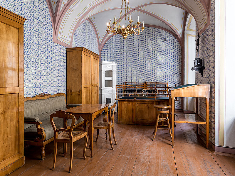 Raum mit Kronleuchter, alten Holzmöbeln, blau gemusterter Tapete und Gewölbe