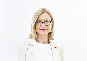 Porträtfoto von Person mit blonden, langen Haaren und weißem Anzug.