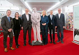 Die Personen stehen in einer Reihe nebeneinander, in der Mitte ein Cutout aus Holz, das Stefan Zweig darstellt. 