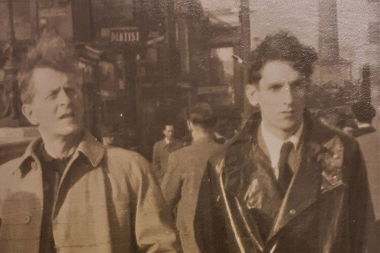 Foto von einem älteren und einem jüngeren Mann in langen Mänteln, die nebeneinander in einer Stadt gehen.
