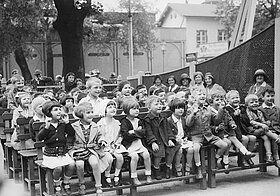 Viele aufgeregte, lachende Kinder auf Zuschauerbänken draußen.