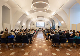 Sitzreihen mit Publikum in Saal.
