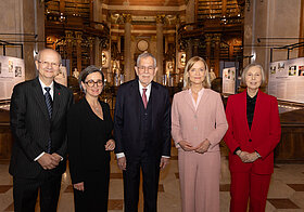 Fünf Personen in Anzügen stehen in Museumsraum.