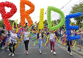Personen mit Regenboden-Luftballon-Flügeln und noch mehr Luftballons, die das Wort "PRIDE" bilden, auf einer Demonstration.
