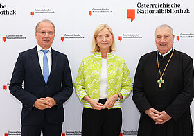 Drei Personen posieren vor Logowand.