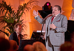 Zwei Personen auf einer Bühne, die singen und Klavier spielen. 