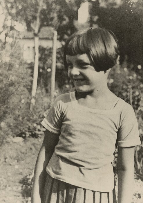 Schwarz-weißes Foto von einem Kind mit kurzen Haaren, lächelnd draußen stehend.