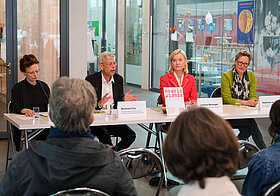 Vier Personen an Podium vor Publikum.