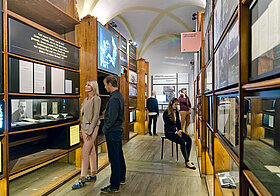 Ausstellungsraum des Literaturmuseums. Personen betrachten Objekte, eine Frau hört mit Kopfhörern ein Audiobeispiel.