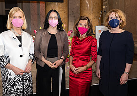 Vier Personen in eleganter Kleidung stehen nebeneinander.