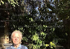 Person in blauem Hemd und Weste sitzt draußen in der Sonne, auf dem Tisch daneben Äpfel.
