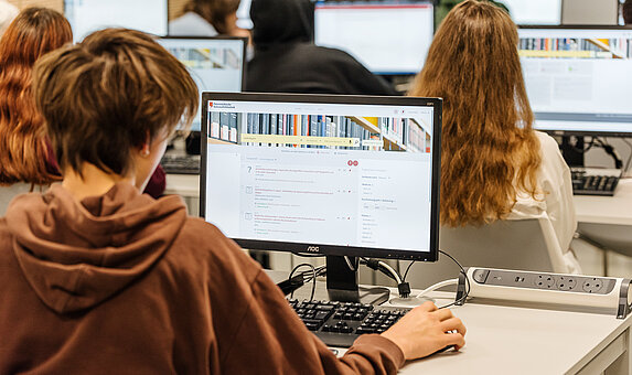 Foto von Person, die an einem Computer arbeitet, von hinten.