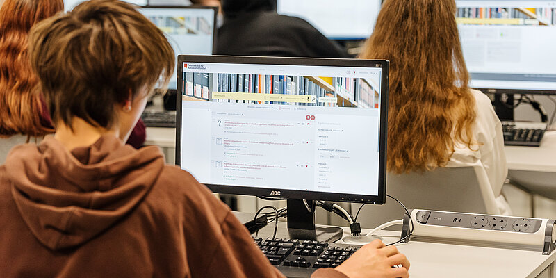 Foto von Person, die an einem Computer arbeitet, von hinten.