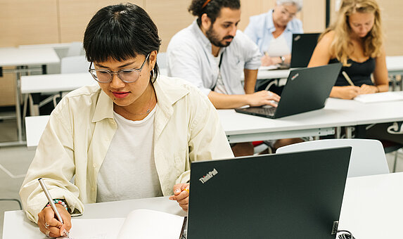 Mehrere Personen sitzen vor Laptops und machen sich Notizen 