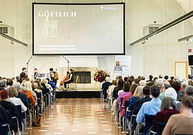 Raum mit Publikum und Leinwand.
