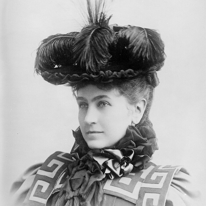 Schwarz-weißes Porträt-Foto von einer Frau mit einem großen Hut mit Federn