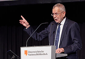 Bebrillte Person im Anzug am Rednerpult.