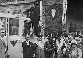 Foto von Personengruppe neben altmodischem Auto, sie tragen ein Schild auf Stoff mit Beethoven darauf.