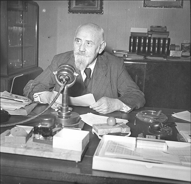 Renner an einem Schreibtisch vor einem Mikrofon sitzend, schwarz-weiß