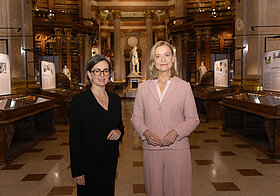 Zwei Personen in Anzügen stehen in Museumsraum.
