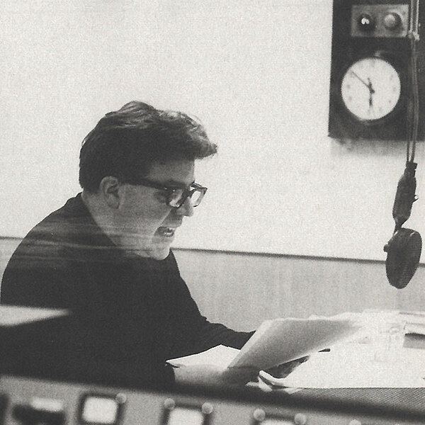 Schwarz-Weißes Foto von Mann mit Zettel, der in ein Mikrofon spricht.