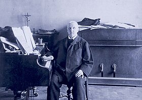 Schwarz-weißes Foto von Person, die an Klavier in einer Wohnung sitzt.