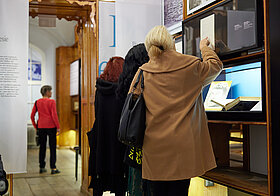 Drei Personen schauen sich ein Dokument in einer Ausstellung an.