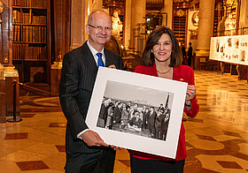 Zwei Personen halten ein schwarz-weißes Foto in Museumsraum.