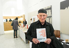 Bodo Hell lächelt in die Kamera und hält in seinen Händen den Museumskatalog.