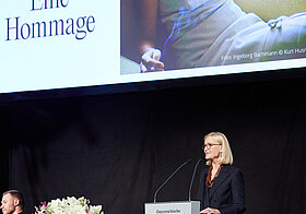 Person am Rednerpult. Dahinter eine Leinwand mit Portrait von Ingeborg Bachmann.  