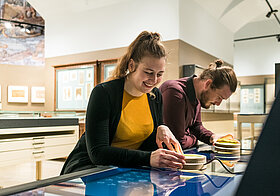 Zwei Personen sehen sich eine Vitrine im Museum an