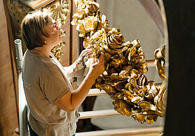 Person bearbeitet vergoldetes Holzornament.