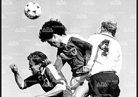 Schwarz-Weiß-Foto von drei Menschen, die Fußball spielen.