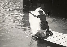 Person wäscht ein Laken in einem Fluss.