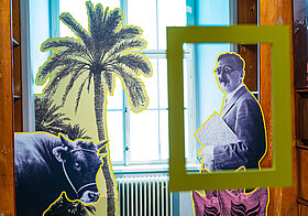 Foto vom Ausstellungsraum. Pappfigur von Stefan Zweig, einer Palme und einem Stier.