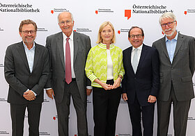 Fünf Personen posieren vor Logowand.