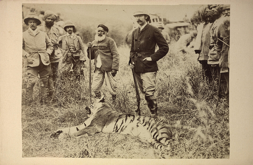 Schwarz-weißes Foto von Person mit Waffe neben einem toten Tiger, rundherum andere Personen.