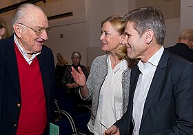 Drei Personen in eleganter Kleidung im Gespräch miteinander.