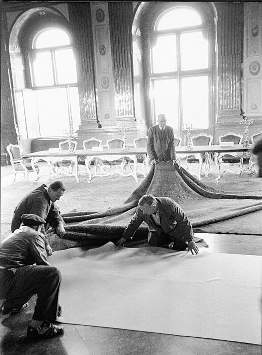 Foto von Personen, die Teppich in großem Saal ausrollen.