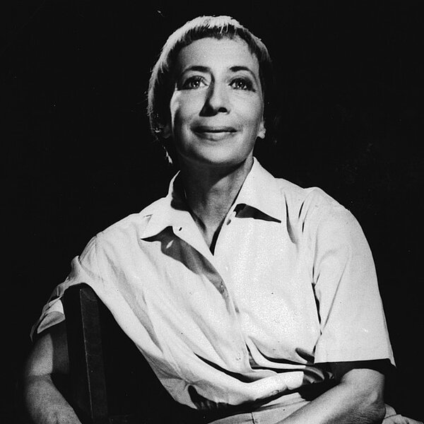 Schwarz-weißes Porträtfoto von lächelnder Frau mit kurzen Haaren aus Sessel posierend